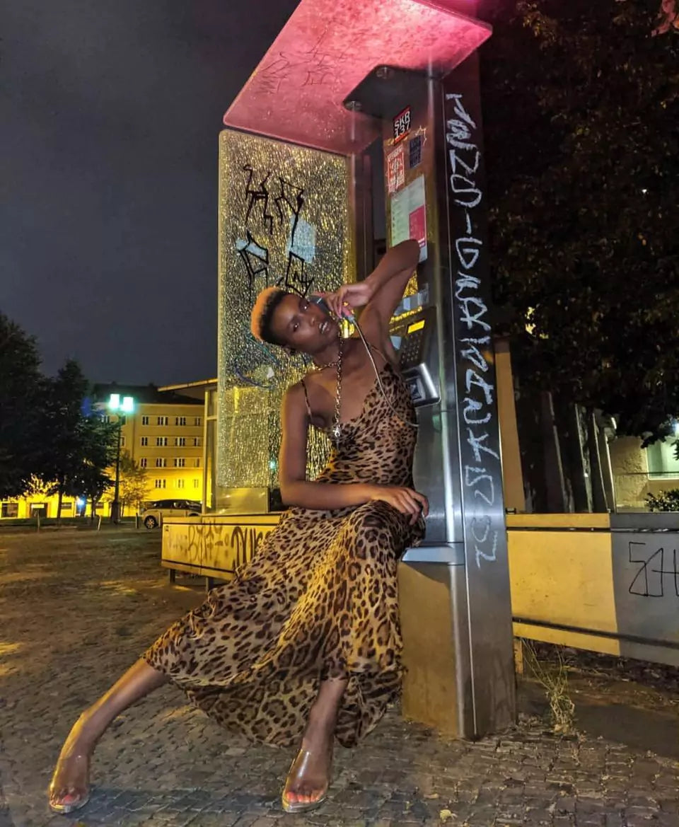 A woman in a leopard print dress posing in front of a phone booth.