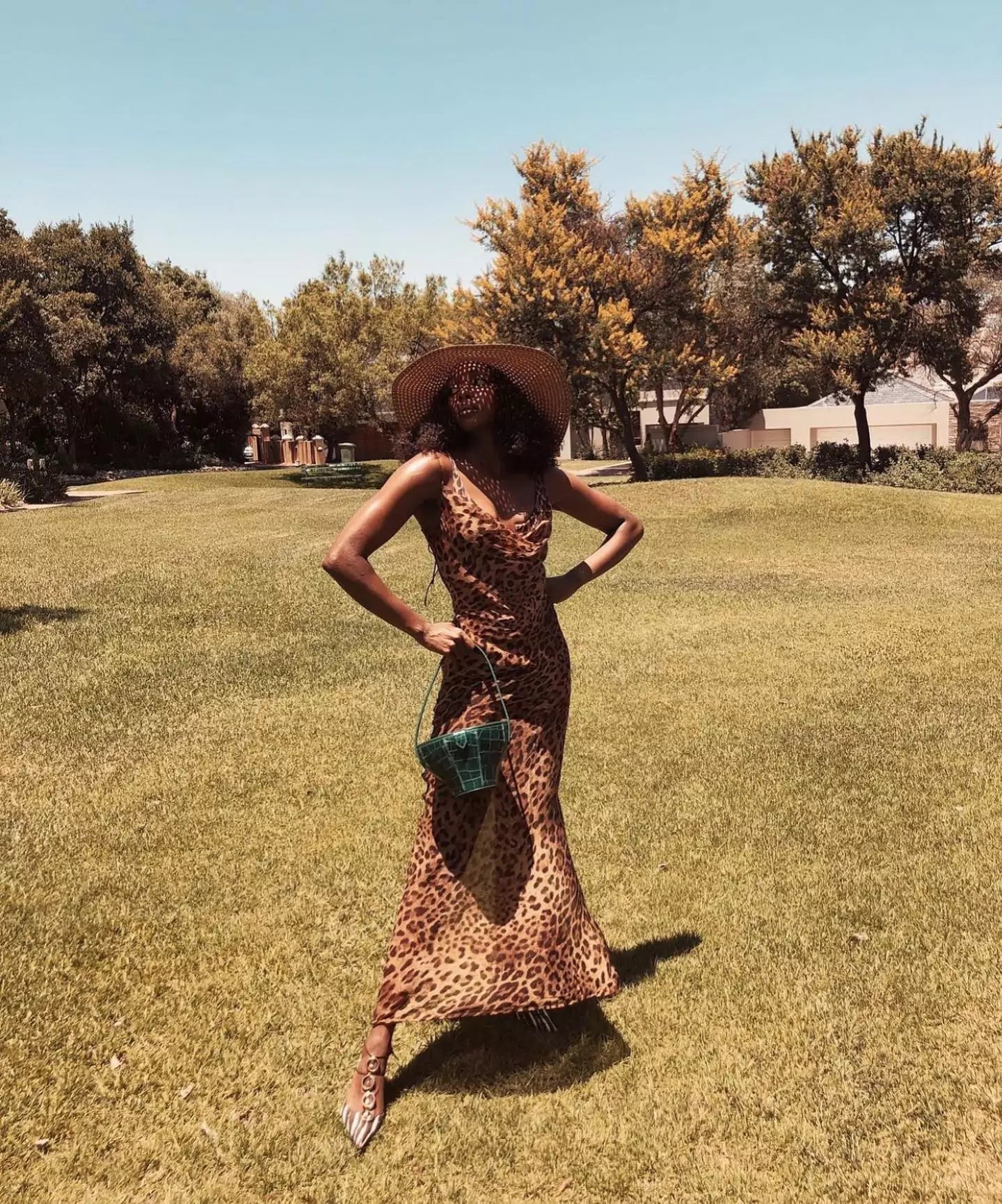 A stylish woman in a leopard print Jinja dress standing gracefully in a park.
