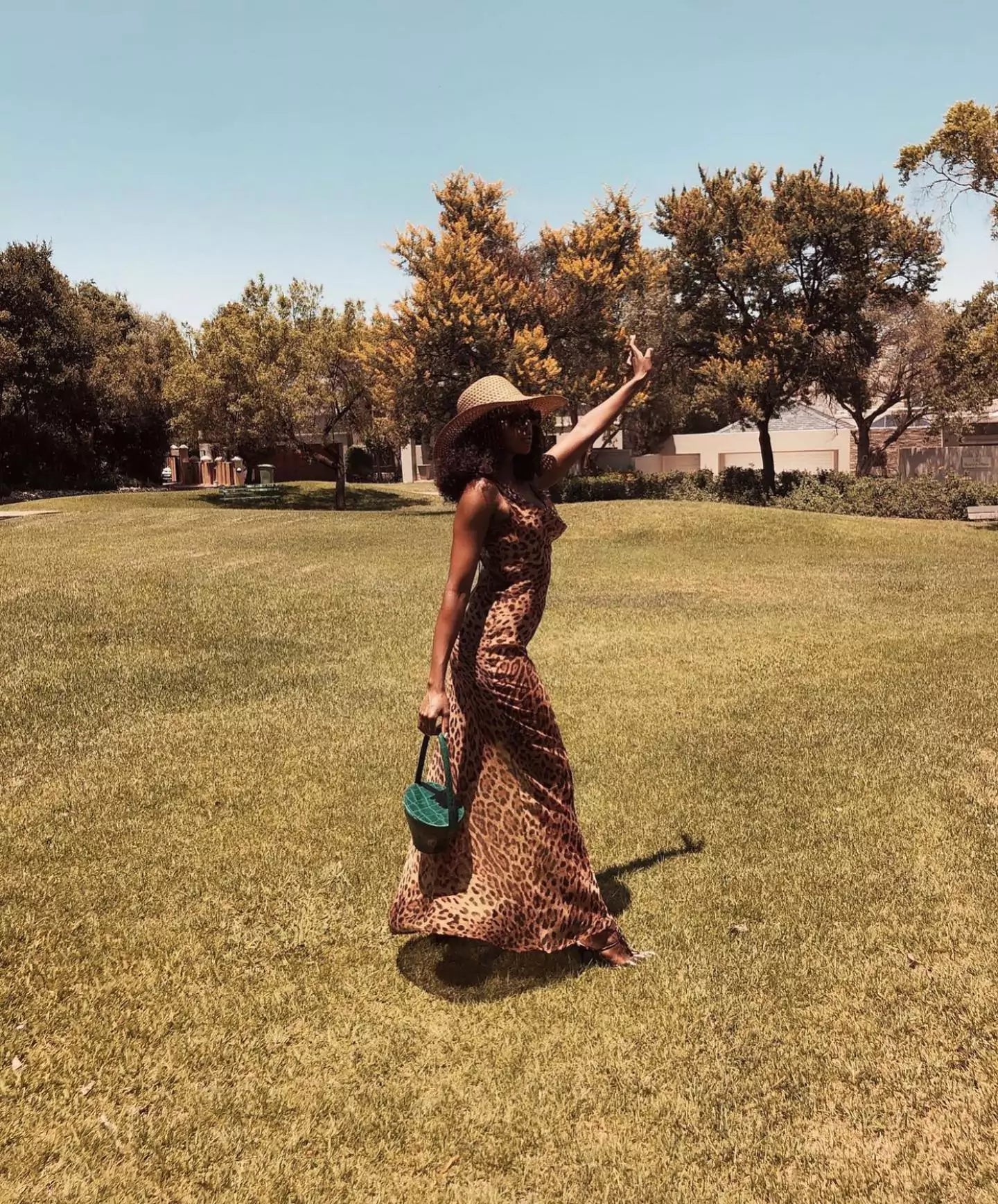 A woman wearing a dress and hat in a park.