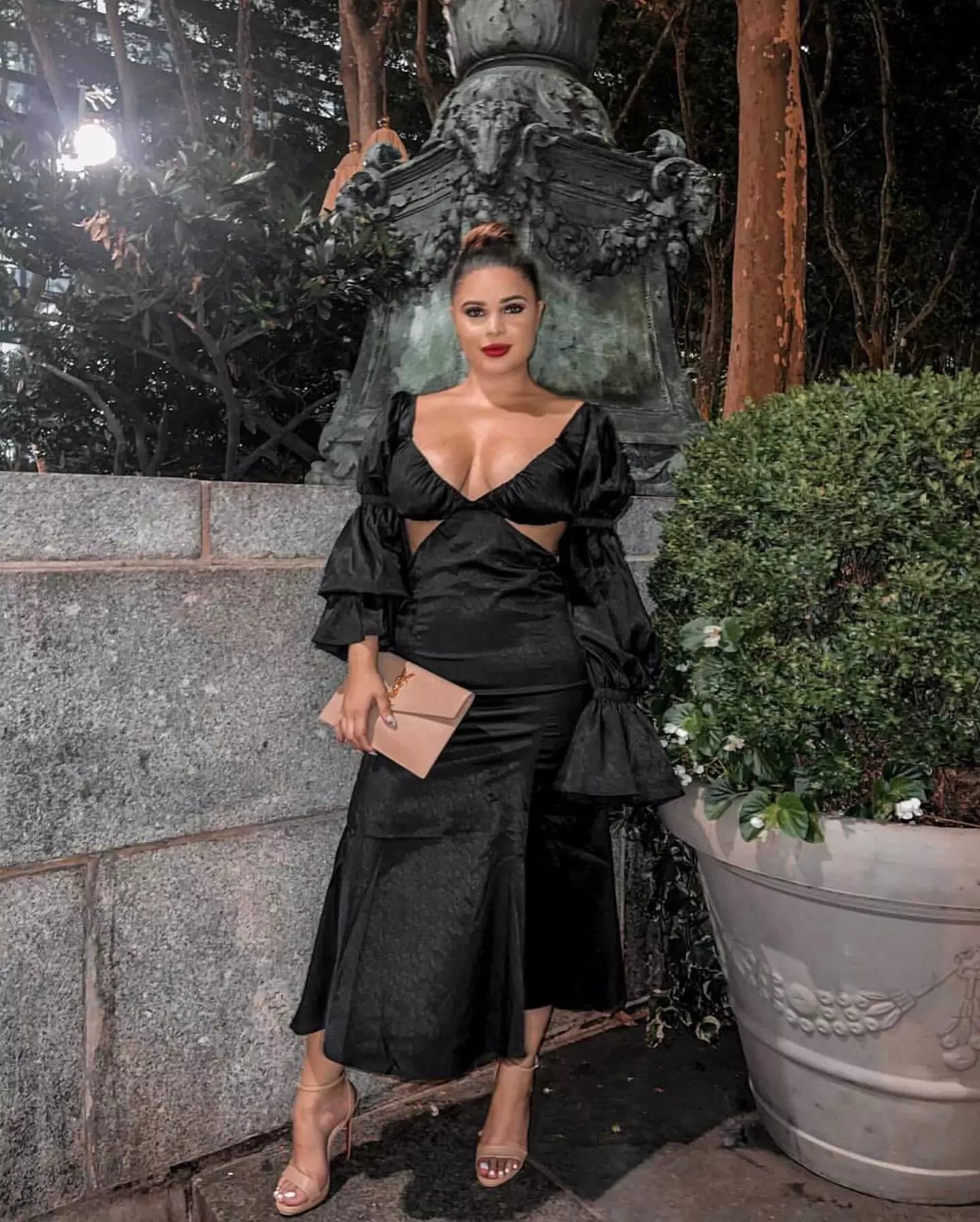 A woman in a black dress posing in front of a fountain.