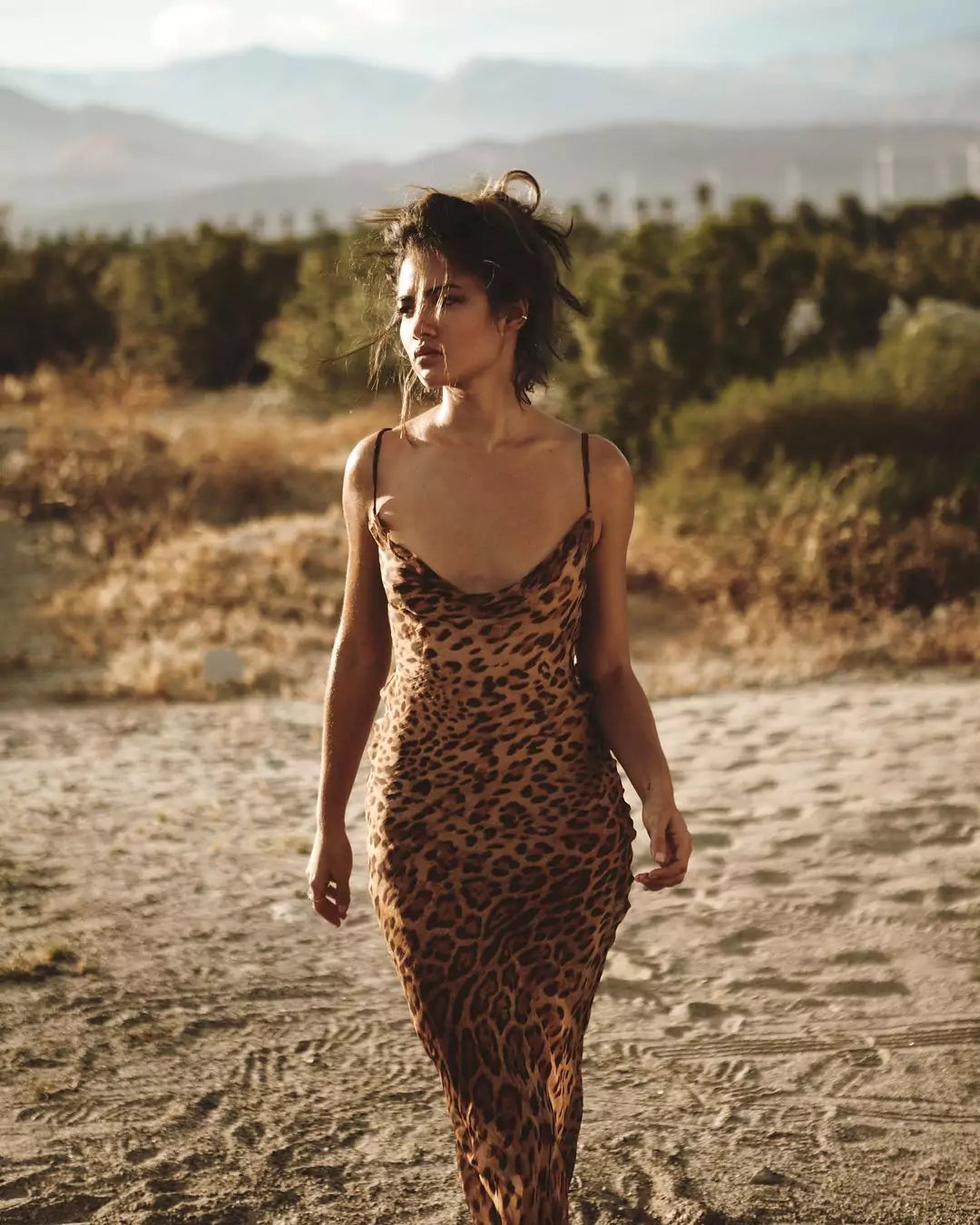 A woman in a leopard print dress walking through the desert.