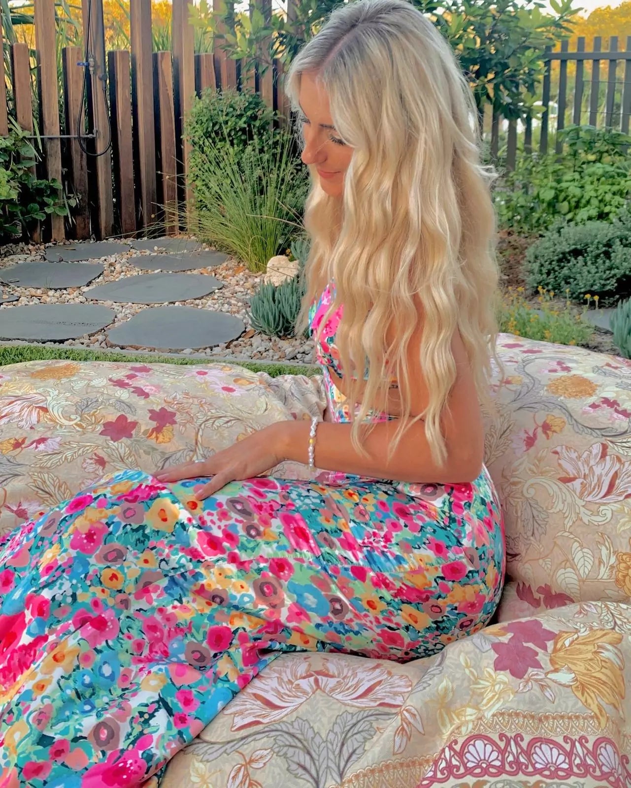 A woman in a floral dress sitting on a bed.