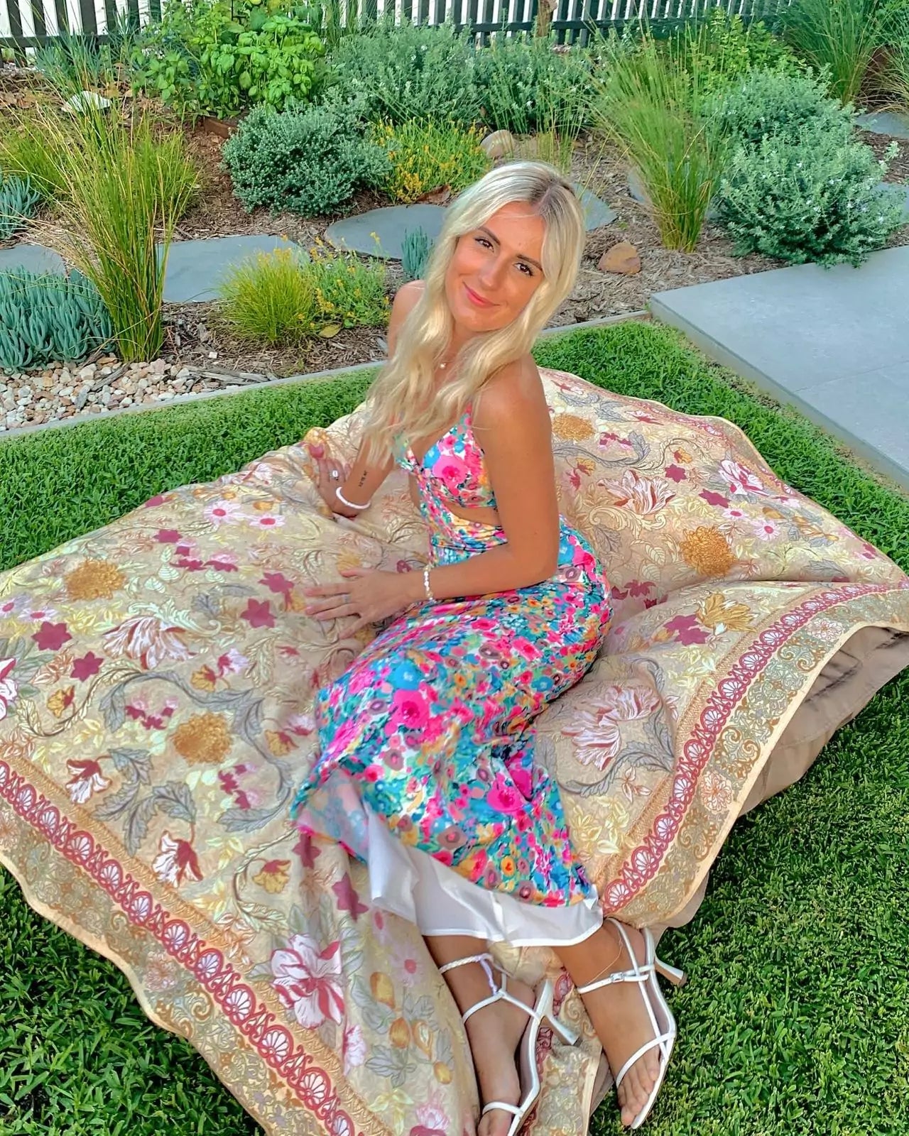 A woman in a floral dress sitting on a blanket.