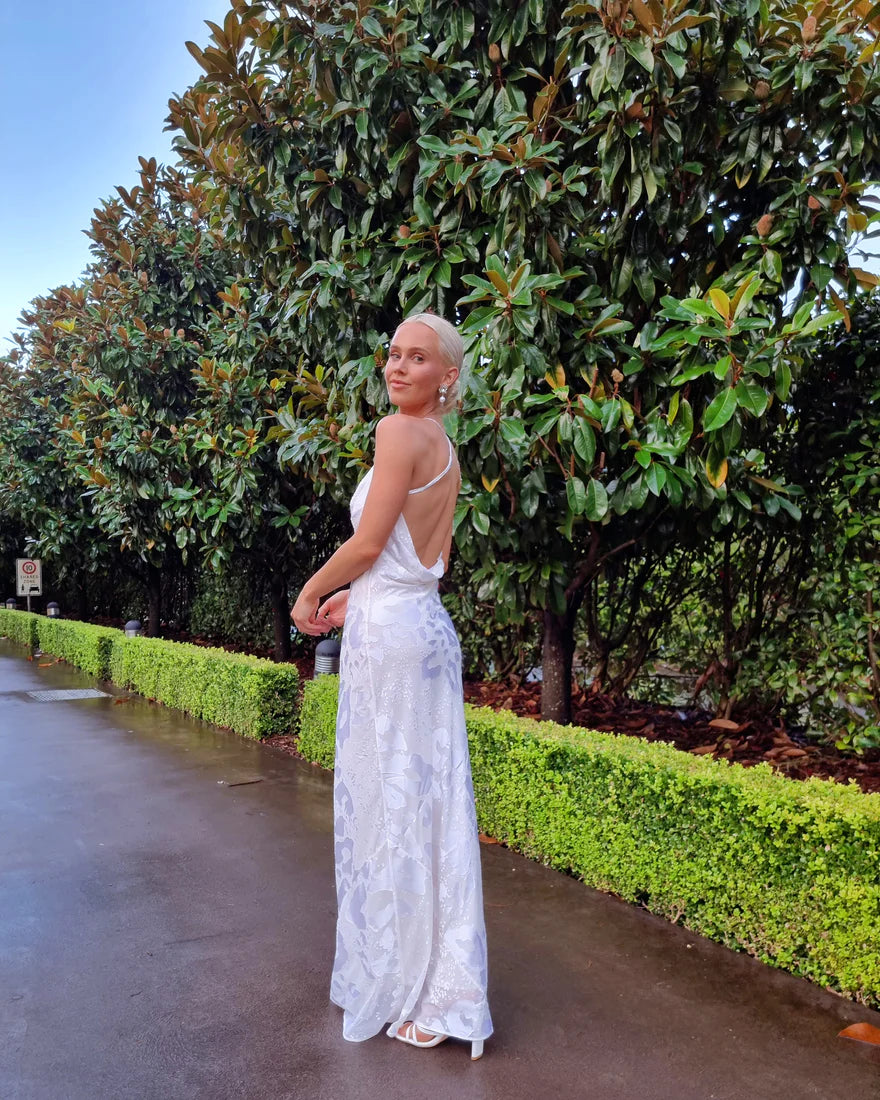 A woman in a white dress standing in front of bushes.