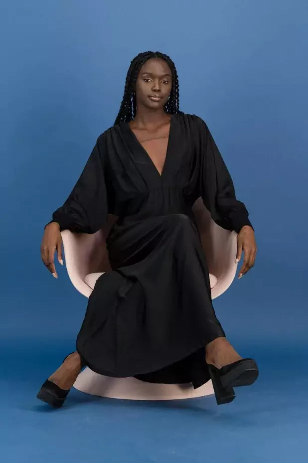 Samiya Black Satin Maxi Dress - Rosey & Vittori's evening look featuring a woman sitting on a pink chair.