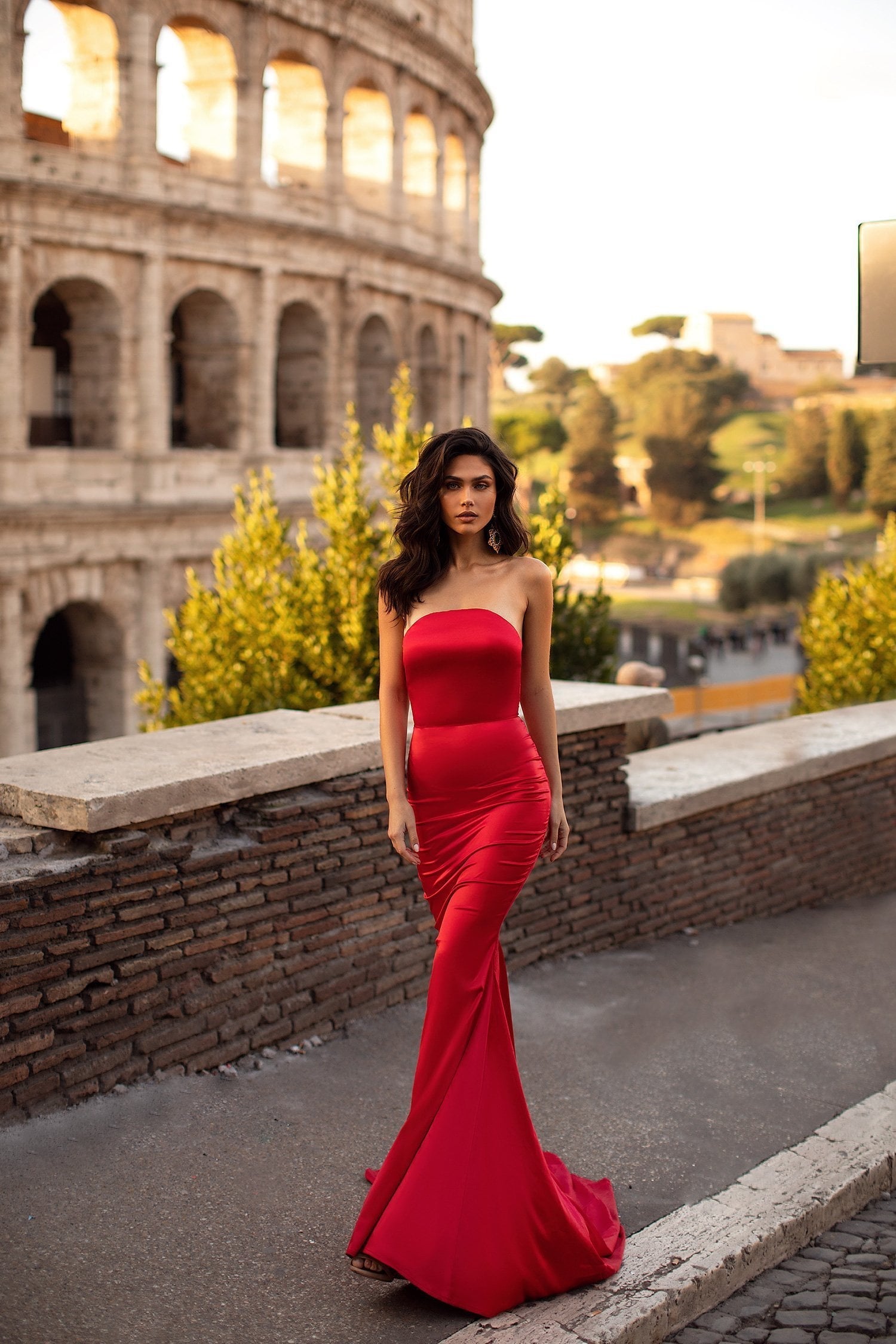 A woman in a red dress is posing in front of the colossion.