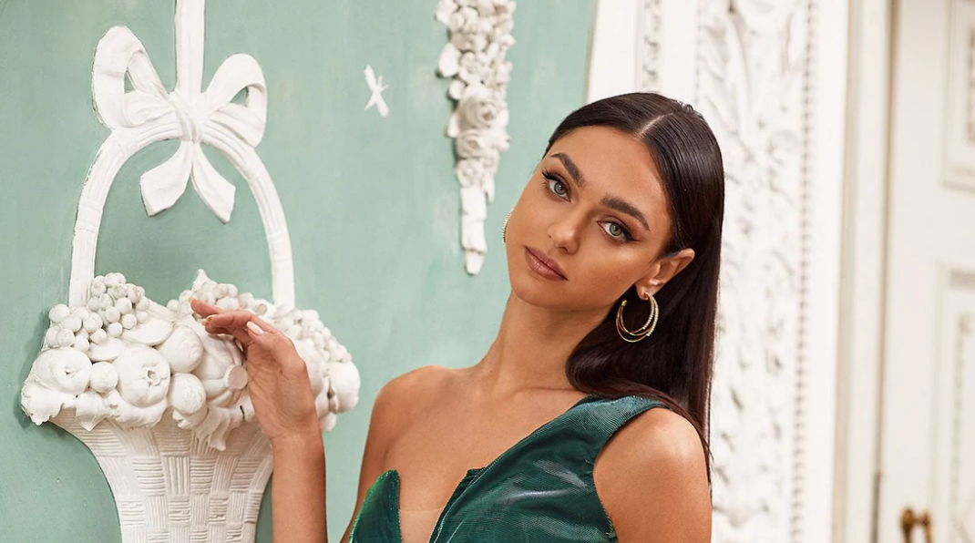 A woman in a green dress posing in front of a white wall.