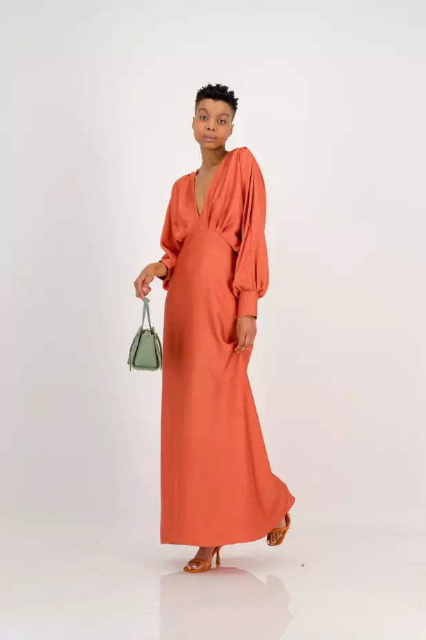 A woman in an orange maxi dress holding a green handbag.
