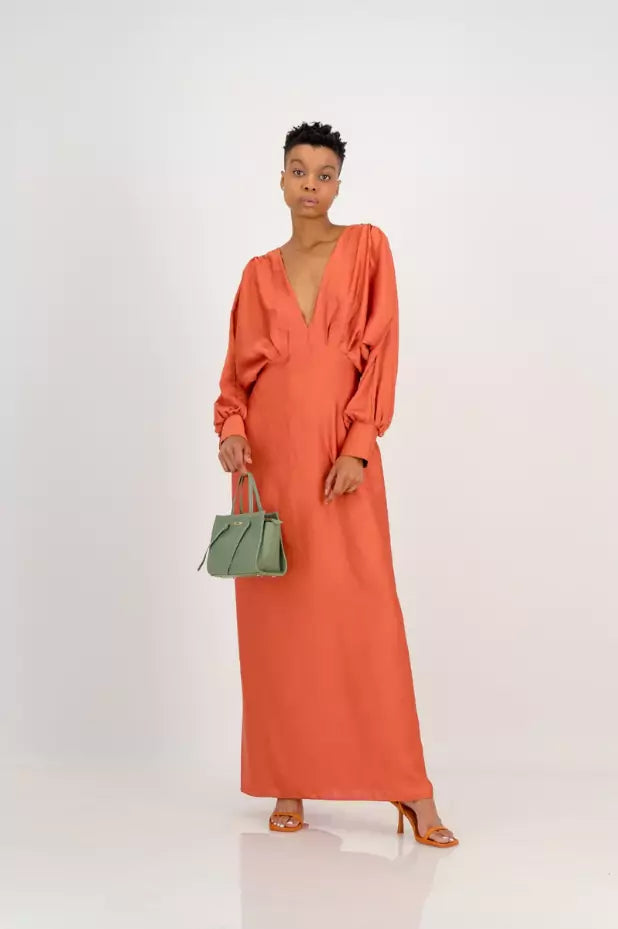 A woman in an orange maxi dress holding a green handbag.