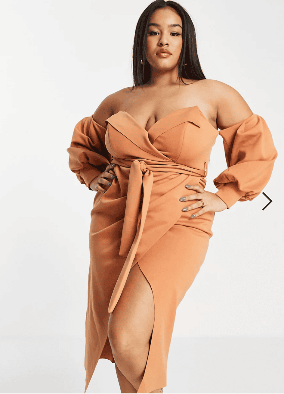 A plus size woman is posing in a tan dress.